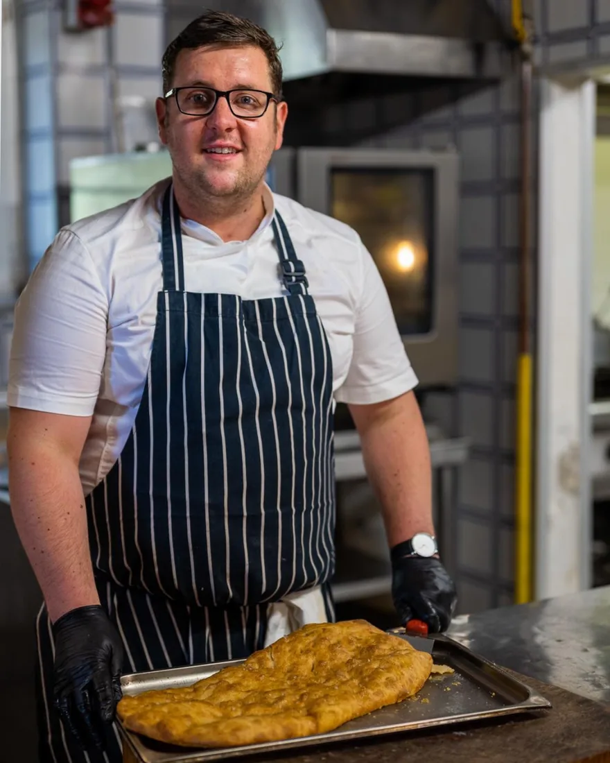 David Thomas, head chef and founder of Pane Olio, lifting a freshly baked tray of focaccia in the kitchen
